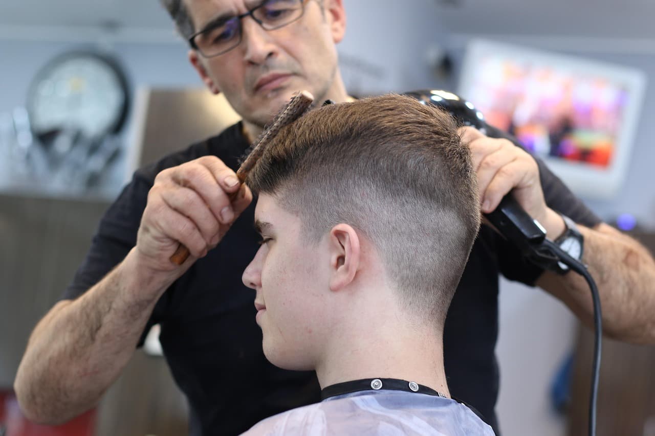 Barber blending a fade with comb and dryer, side of the head close up